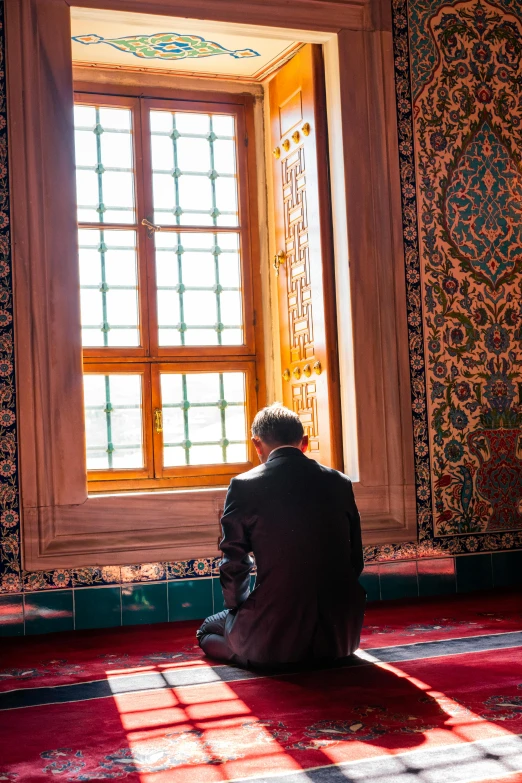 a man prays while sitting on a floor under a window