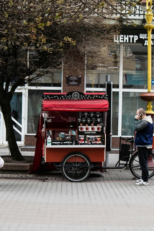 a man on a phone next to an ice cream cart