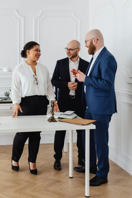 two men and a woman stand at a white table