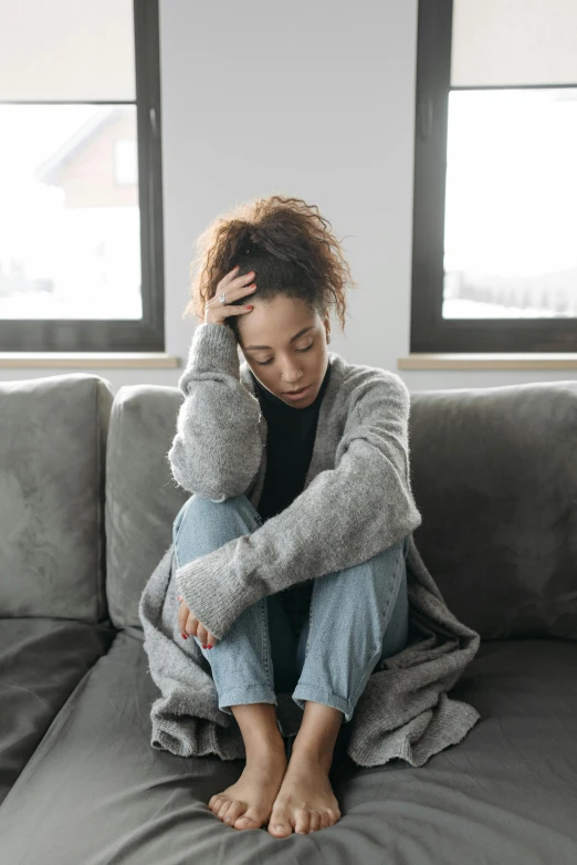 a woman sitting on a couch while holding her hand to her hair