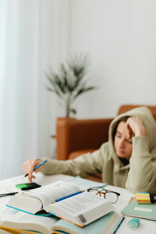 a person in a hooded jacket sitting at a table with an open book