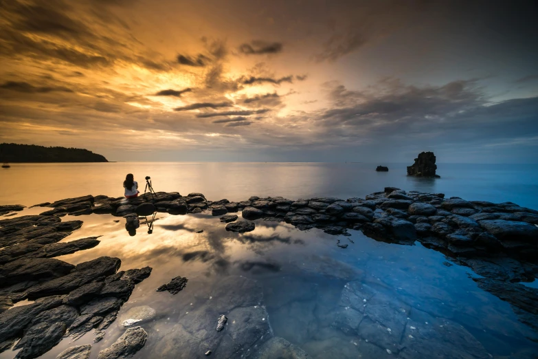 an image of a couple standing on the rocks at sunset