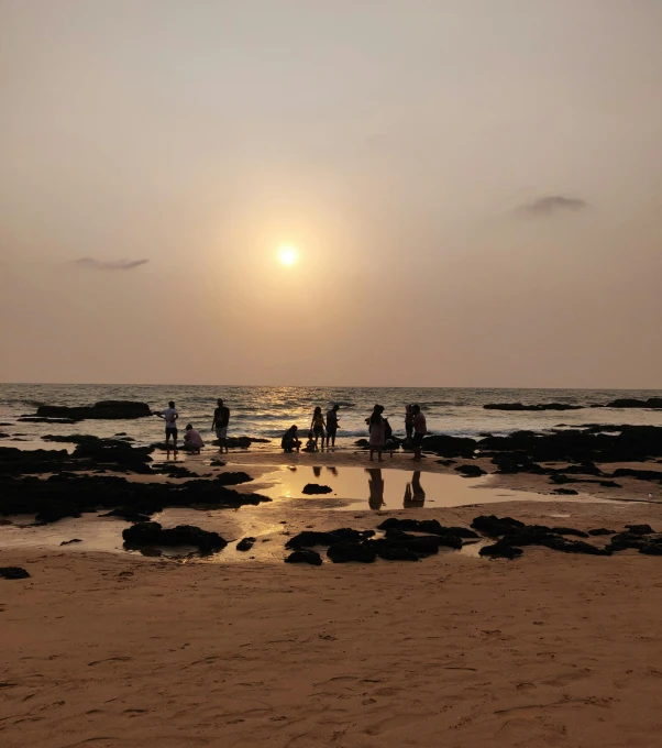 people walk along a shoreline at sunset