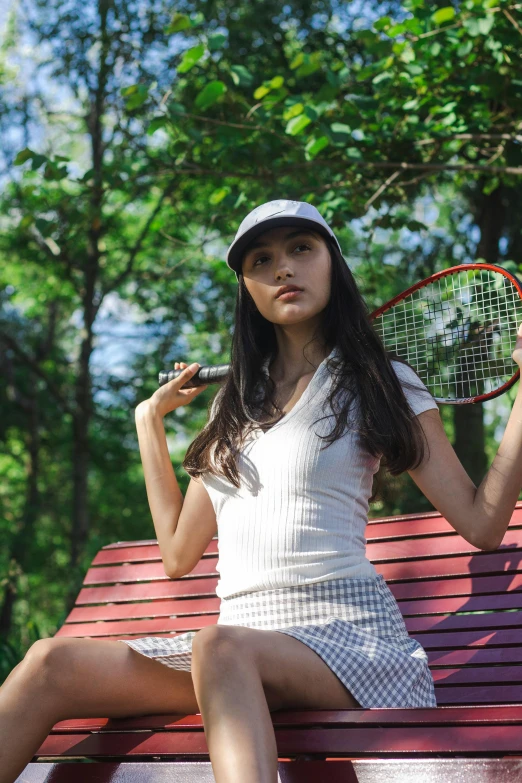 a girl wearing a tennis skirt and shirt sits on a park bench with her tennis racket