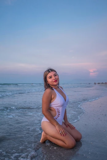 a woman sitting on the beach while in a white swimsuit
