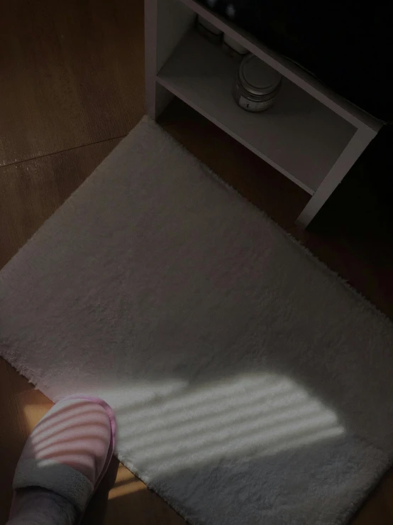 a white rug is sitting on a hardwood floor with shoes in the light from behind it