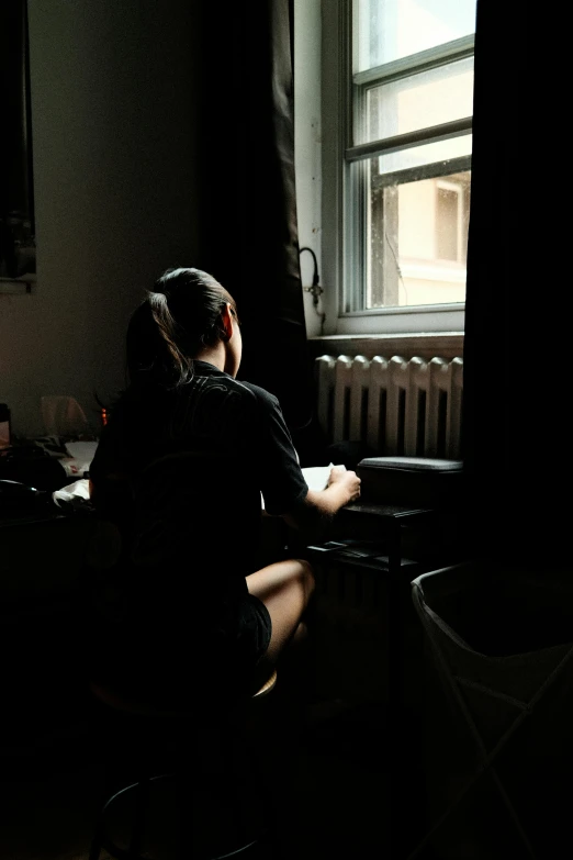 a woman sitting down in a darkened room next to a window