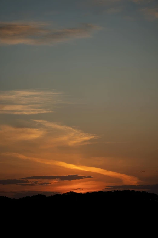 a bright orange sky with some clouds on a hill