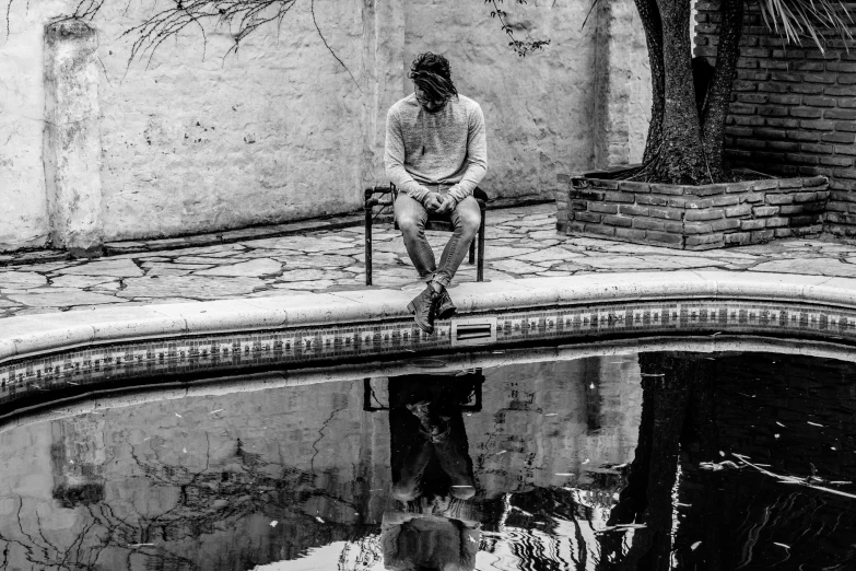 a man sits alone and looks off into the distance near a pool