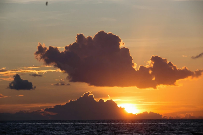 the sun is going down over a cloudy ocean