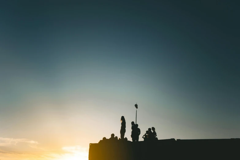 several people stand on top of a building at sunset