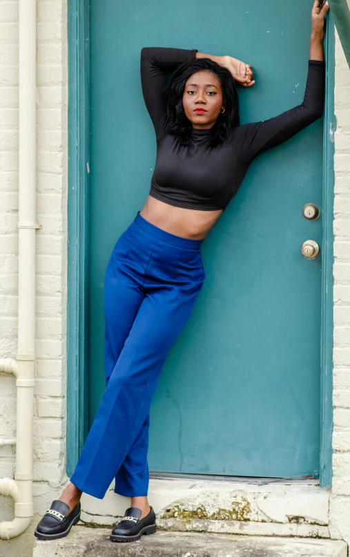 the woman poses in front of a door wearing blue pants