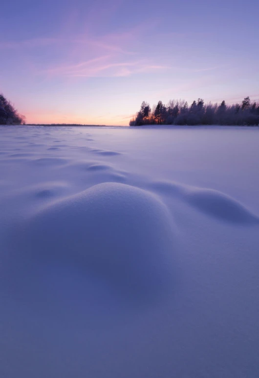 sunset and snowy riverbank with trees in background