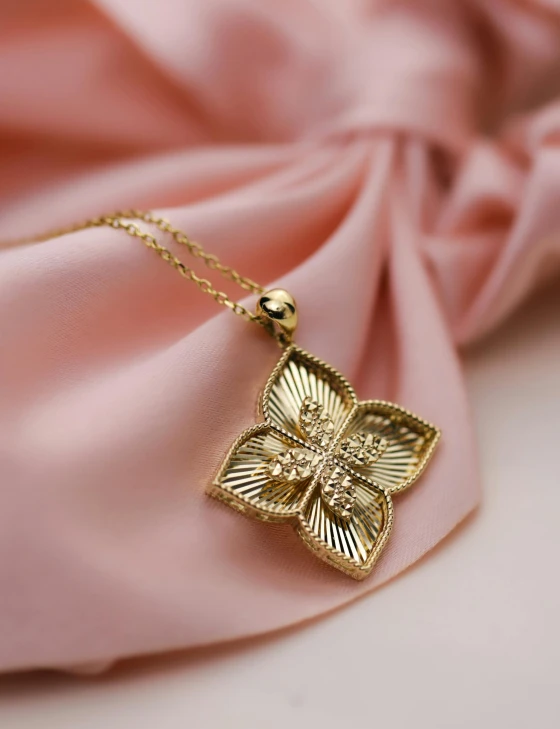 a gold pendant with a flower is placed on a pink fabric