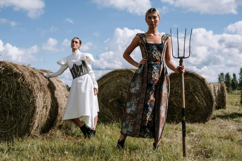 two woman in dresses pose in front of a bale of hay