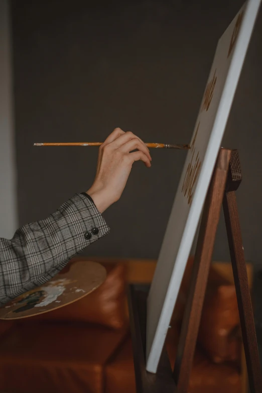 a person's hand holding a paintbrush over an easel