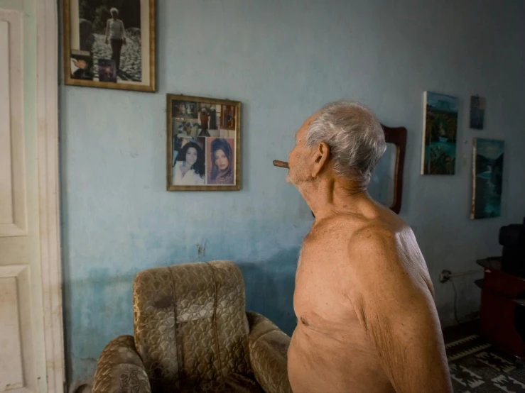 an older man sitting in a chair next to framed pictures