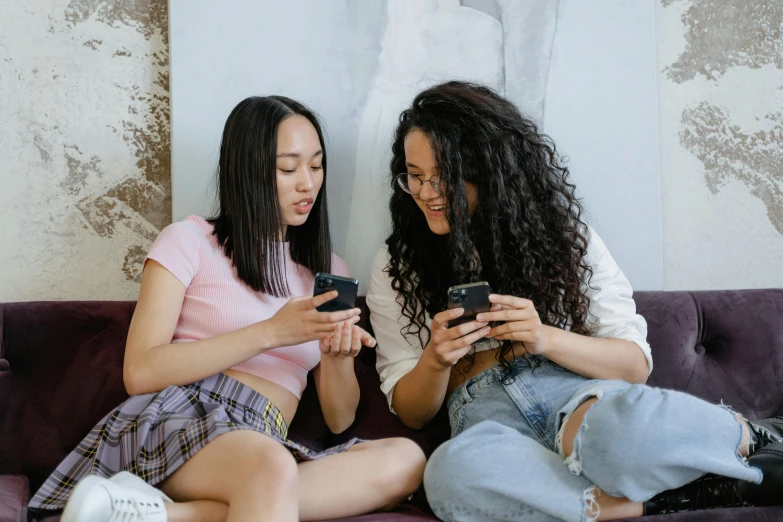 two women are sitting down while looking at their phones