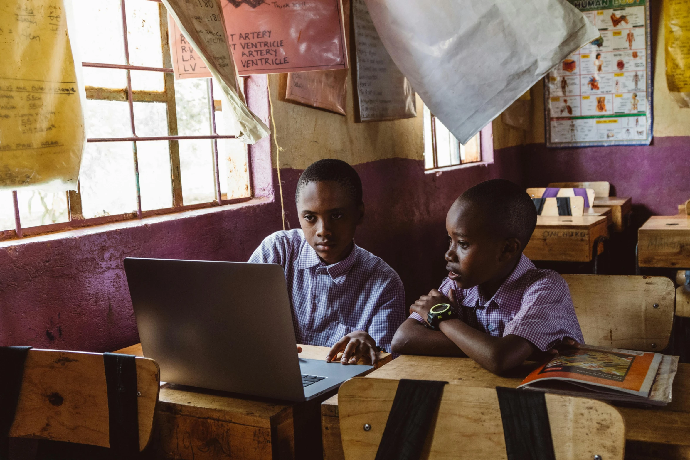 two s work on laptop computers inside of school classrooms