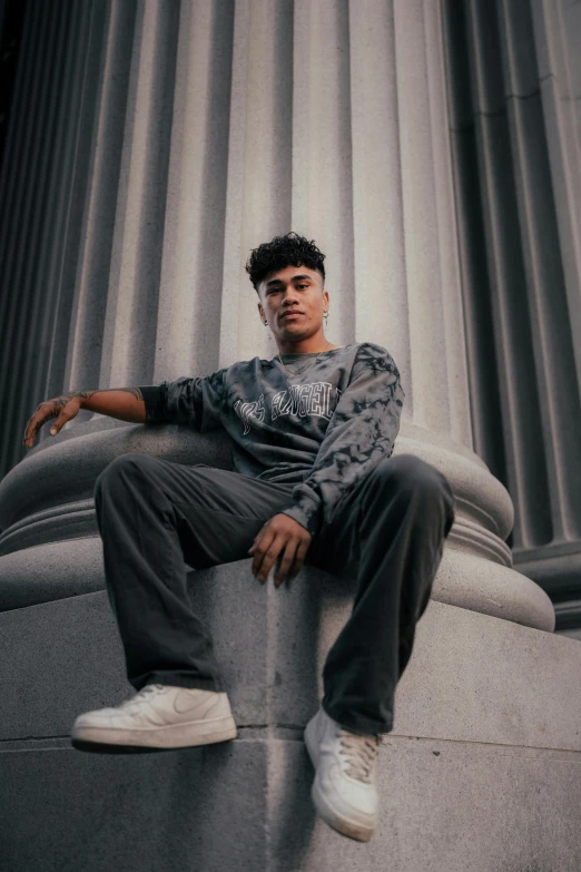 a young man sitting on the side of a building next to a column