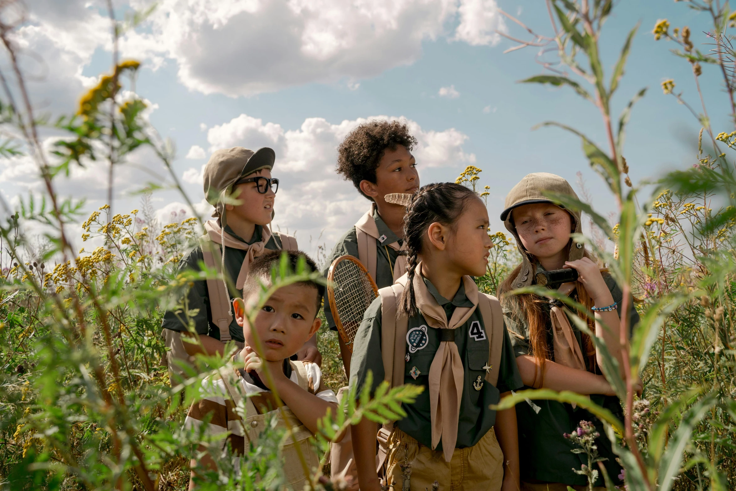 children with backpacks and camping gear stand in tall grass