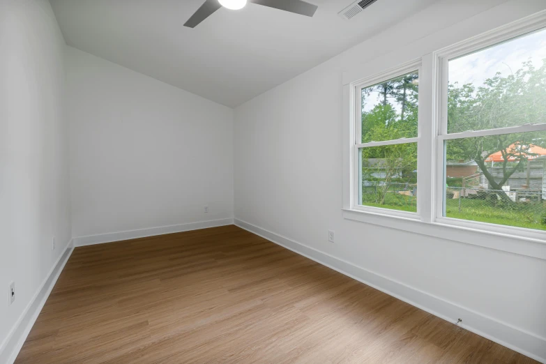 an empty room with two windows and wooden flooring