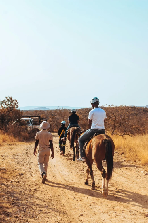 four men on horseback walk on dirt road in desert