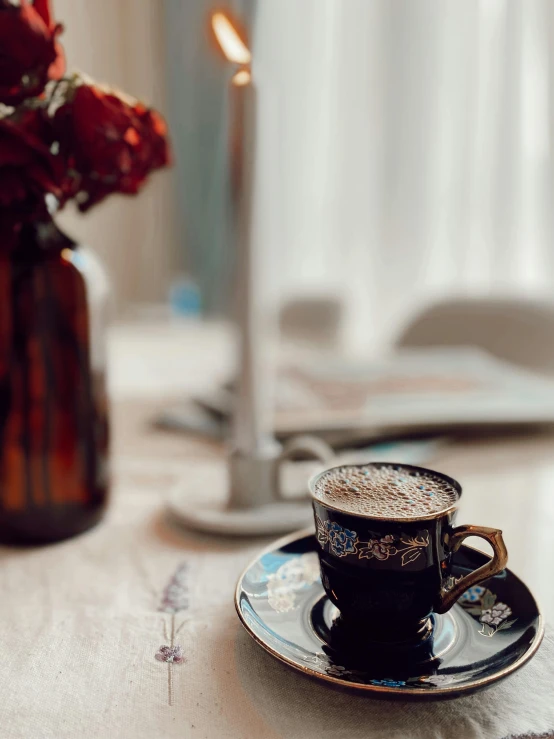 a cup on a saucer near a lit candle and flowers