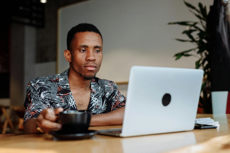 a young man is sitting at a desk and looking at the laptop