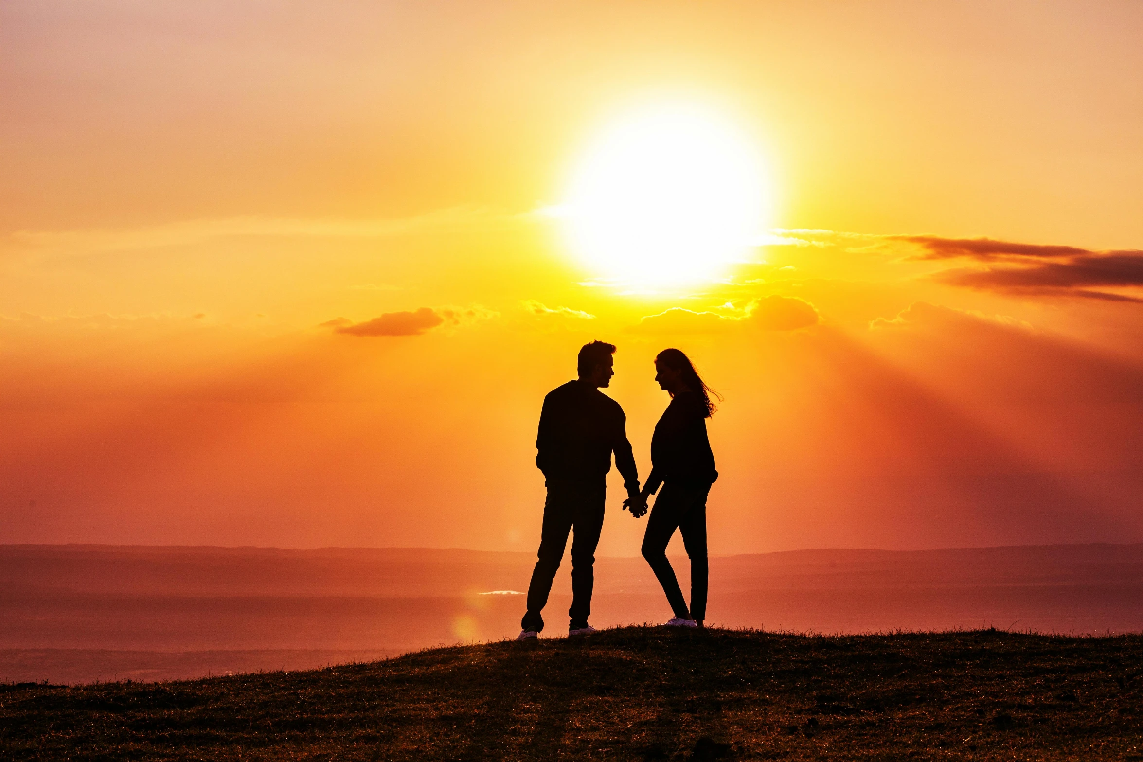 two people are standing on top of a hill under the setting sun