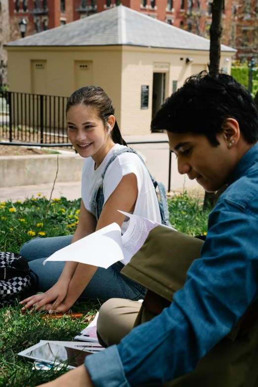 two people sitting on the grass near the grass and paper