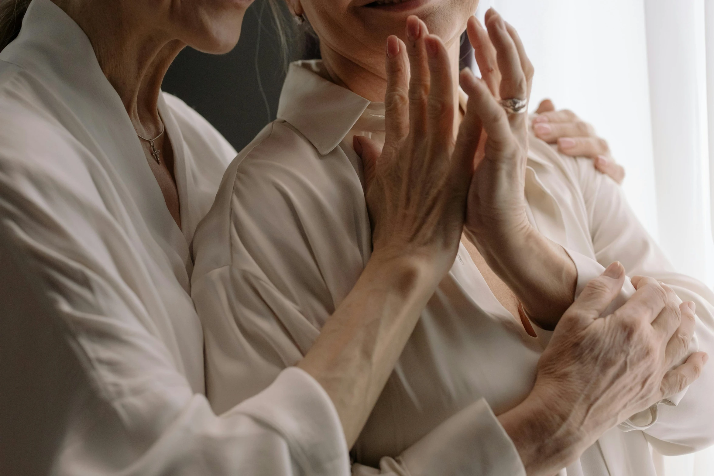 two women standing in front of a window touching hands