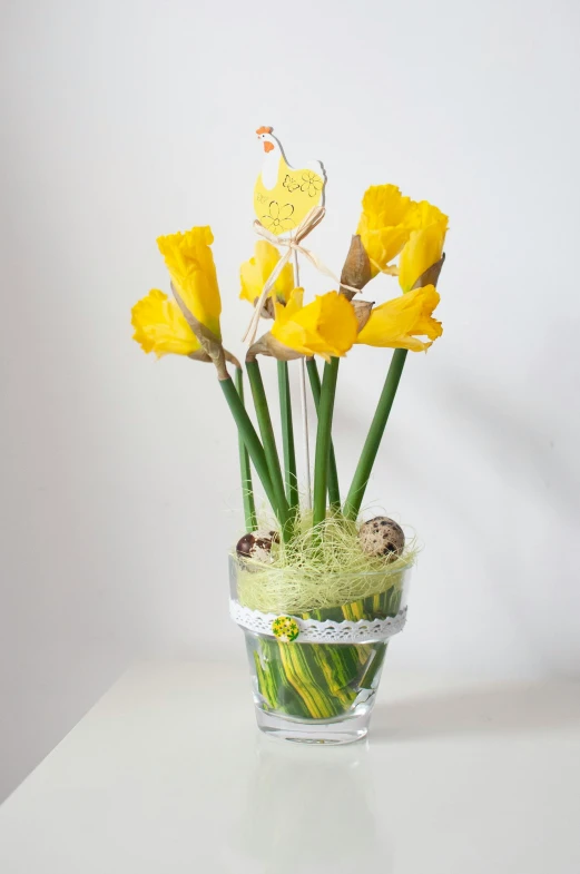 a clear vase holds tulips, moss and a erfly on top