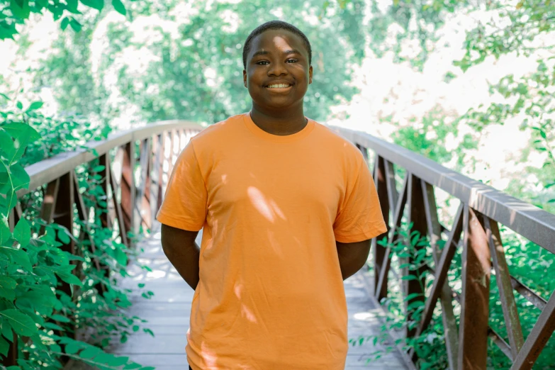 a guy with an orange shirt standing on a wooden bridge