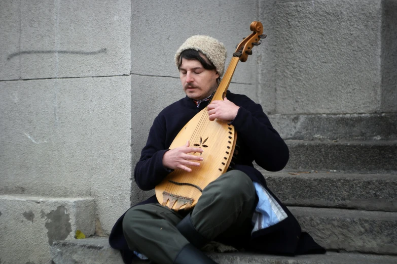 a person sitting in front of a building with a instrument on his lap