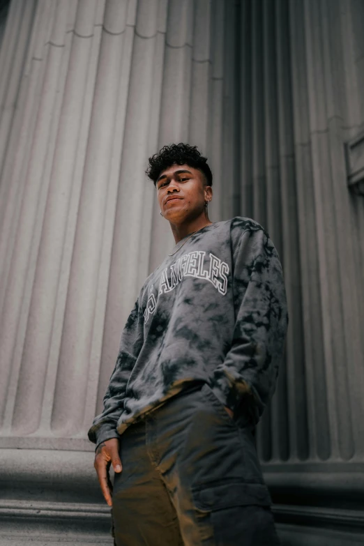 the man standing in front of a pillar is wearing a tie - dye sweatshirt