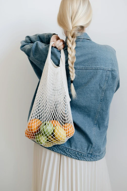 a woman in a long dress holding an un - looped bag filled with fruit