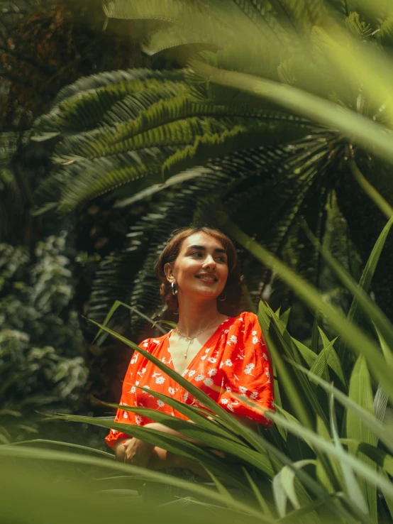 a woman in an orange top is standing among greenery