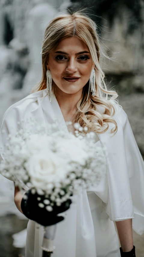 the blonde bride poses in white dress by the waterfall