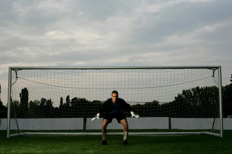 a young man in a uniform prepares to catch a soccer ball near the goal