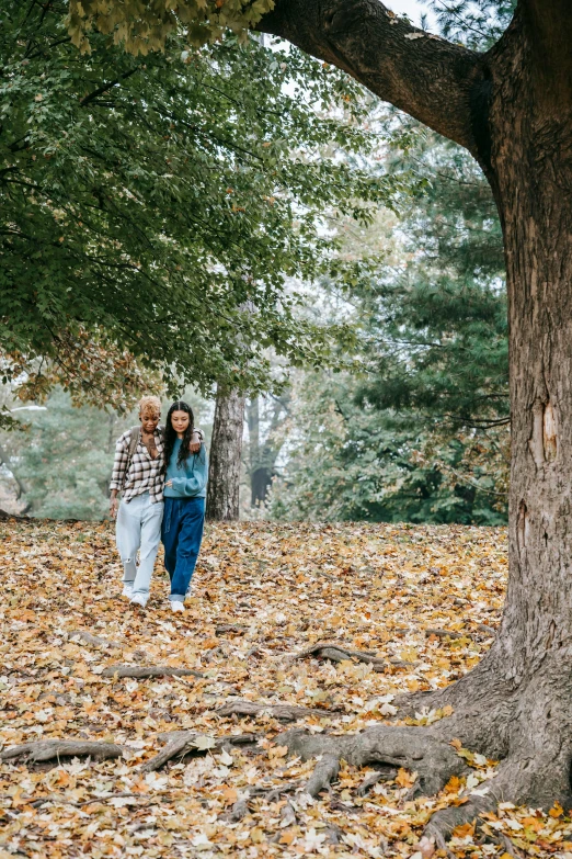 two girls are walking in a park next to trees