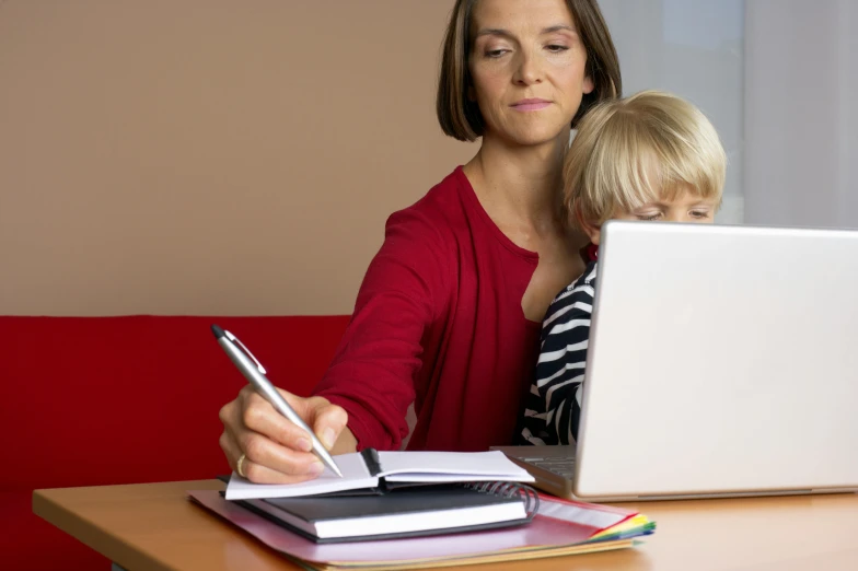 a woman is looking at her child while she holds a pen and writes on paper