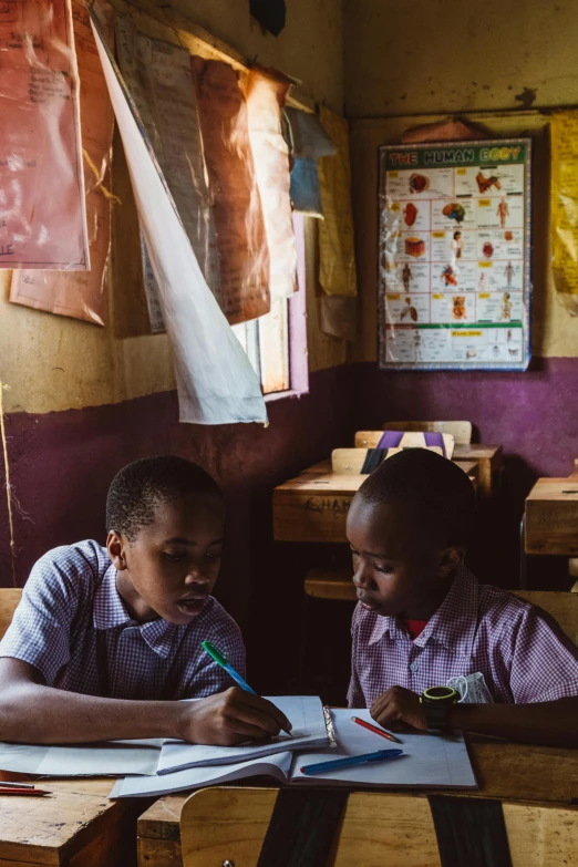 two young children sitting at desks in classroom with paper