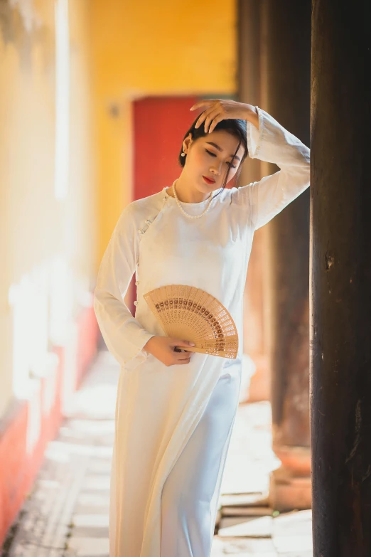 a woman in white clothing standing near a pillar