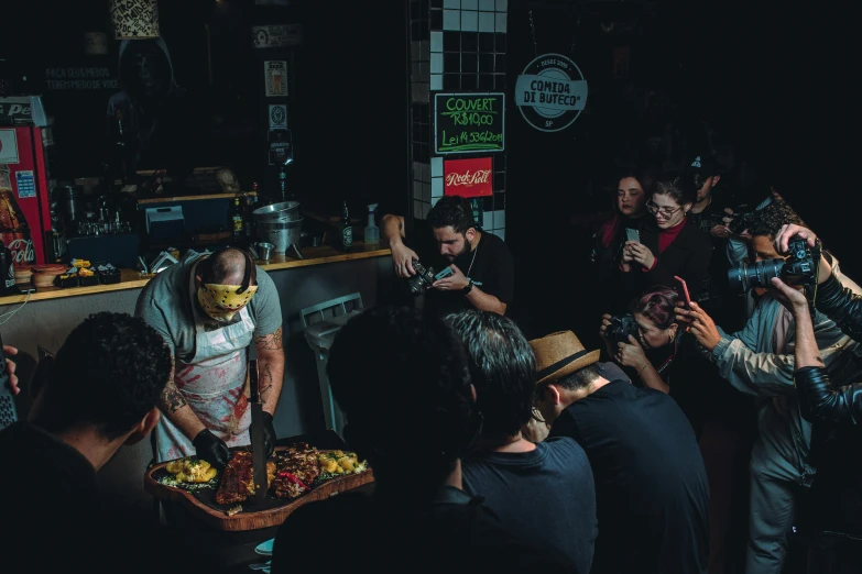 a group of people gathered around the bar, one person holding up a plate of food