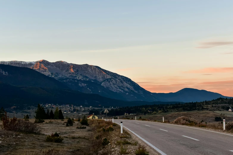 a road in the mountains with sun rising over the mountain tops