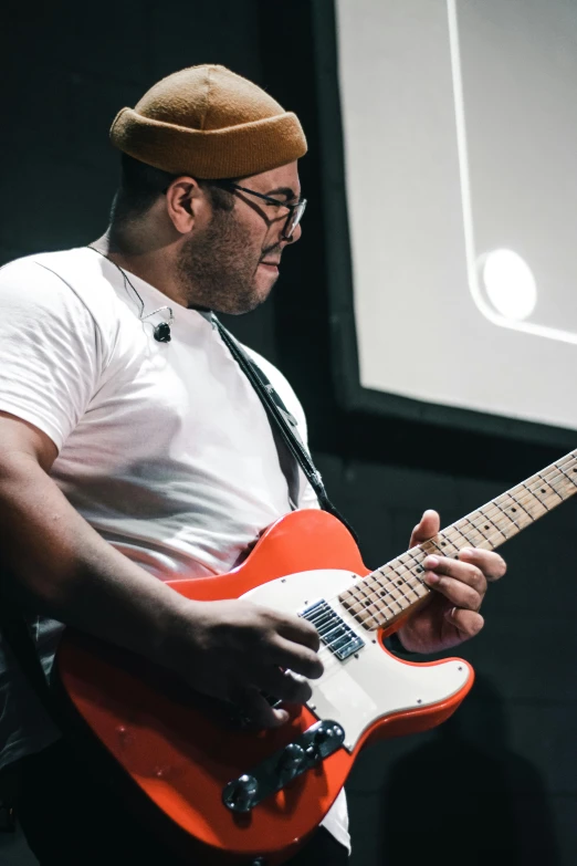 a man wearing glasses plays an orange guitar