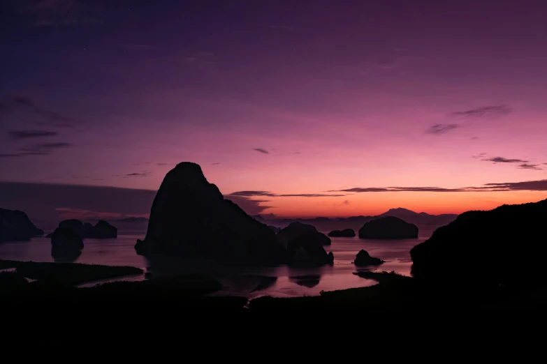 a sunset with some rocks in the water and purple sky