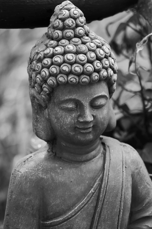 a statue is shown sitting outside, with a bush in the background