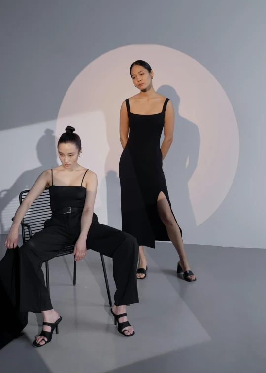 two models in black dresses, one posing on a chair